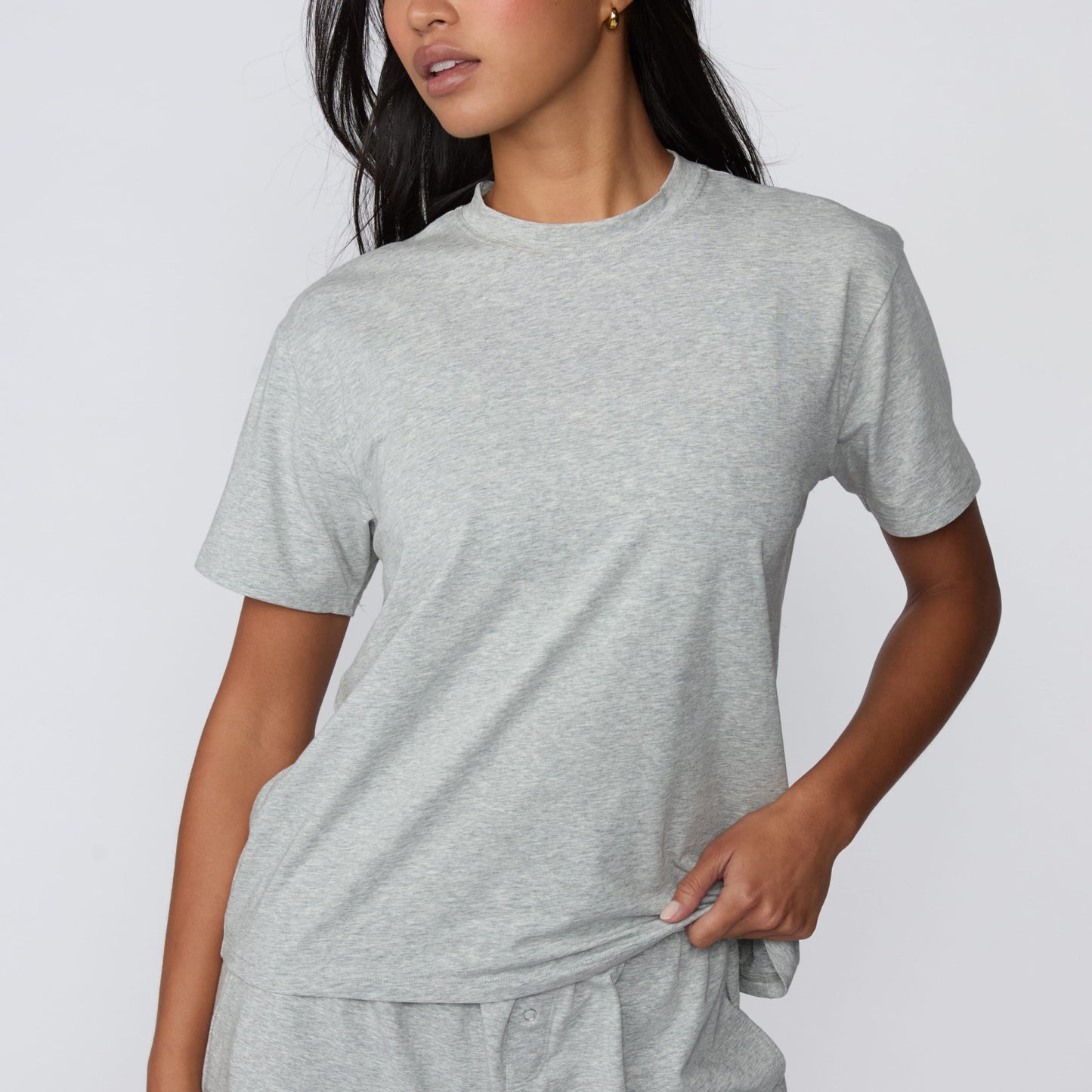 On a light gray studio backdrop, Amber wears the Cloud Cotton Pajama Shirt in Heather Grey with matching pajama shorts. The close-up front view showcases the relaxed fit, crew neckline, and lightweight cotton fabric.