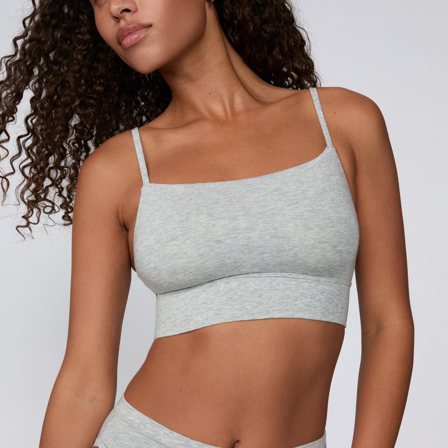 On a light gray studio backdrop, Courtney wears the Cloud Cotton Thin Strap Bralette in Heather Grey with matching underwear. The square-crop close-up highlights the straight neckline, thin adjustable straps, and wide underband.