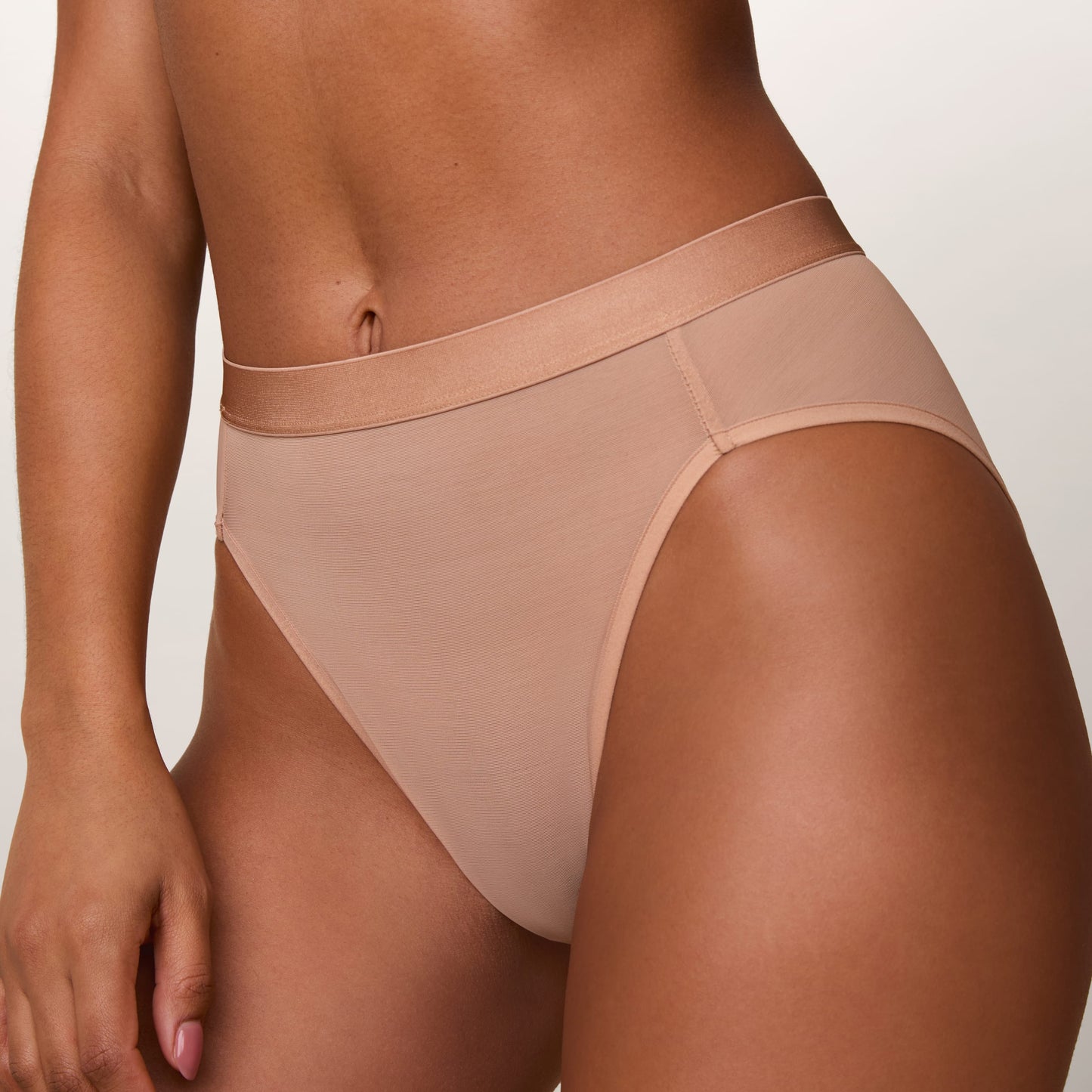 On a light studio backdrop, Ally wears the ComfortMesh™ Highwaist Brief in Taupe. The close-up view highlights the soft sheer mesh fabric, high-rise silhouette, and smooth wide waistband.