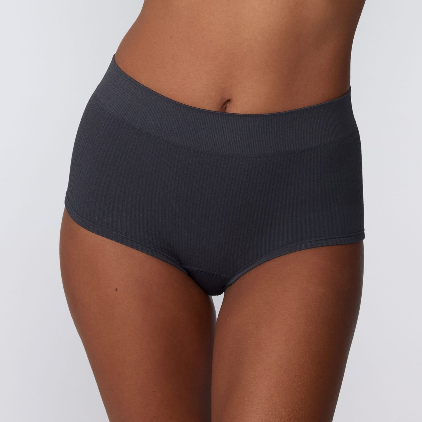 In a studio setting, Courtney wears the Ribbed Seamless Boyshort in Charcoal. A close-up front view highlights the high-rise waistband, full-coverage boyshort silhouette, and ribbed texture.
