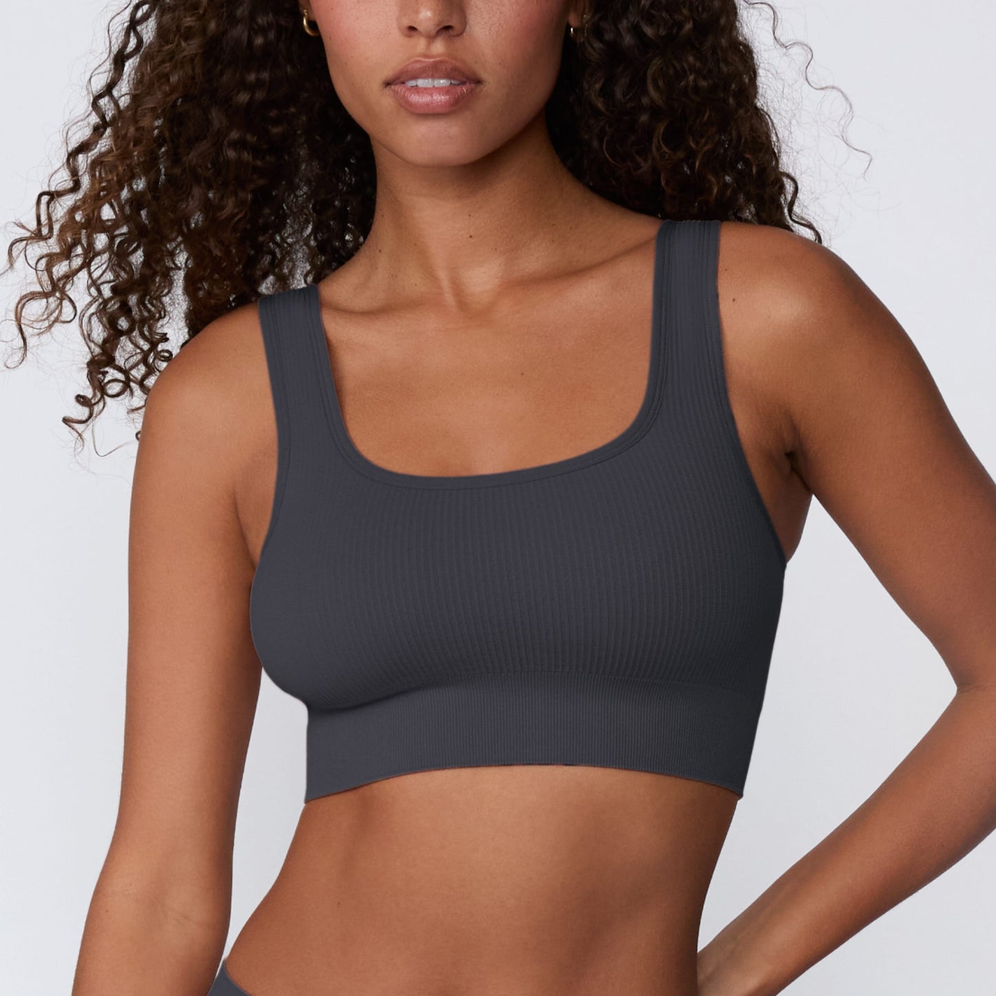 On a light gray studio backdrop, Courtney wears the Ribbed Seamless Scoop Bralette in Charcoal. A close-up front view highlights the scoop neckline, wide straps, ribbed texture, and supportive underband.