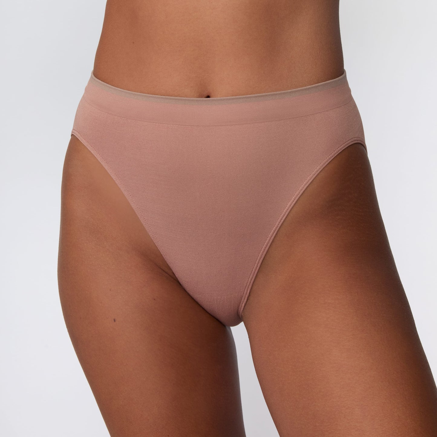 On a light gray studio backdrop, Courtney wears the Smooth Seamless Brief in Plum. A close-up front view highlights the high-leg silhouette, smooth fabric, and contrast trim waistband.