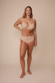 On a neutral studio backdrop, Sonnie wears the Base Lace T-Shirt Bra in Beige with matching underwear. The full-body view showcases the bra’s smooth cups, underwire construction, adjustable straps, and coordinating lace-trim underwear.