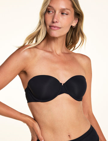 Against a white studio backdrop, Meagan wears the Base Strapless Bra in Black with matching underwear, showing the smooth strapless silhouette and supportive molded cups. sizing: Meagan wears size 34B