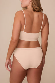 On a neutral beige backdrop, Sonnie wears the Bliss Bikini in Beige, shown from the back to highlight the full back coverage and smooth, clean finish.