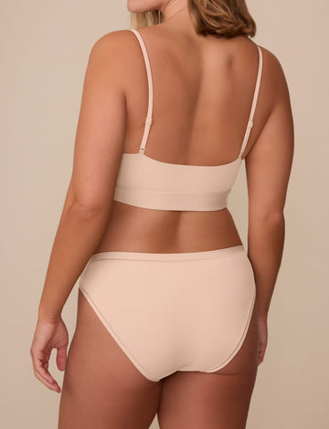 On a neutral beige backdrop, Sonnie wears the Bliss Bikini in Beige, shown from the back to highlight the full back coverage and smooth, clean finish.