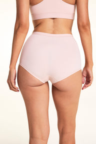 On a light studio backdrop, Meagan wears the Bliss Boyshort in Ember Rose, shown from the back to highlight the full-coverage fit, smooth fabric, and clean leg openings.