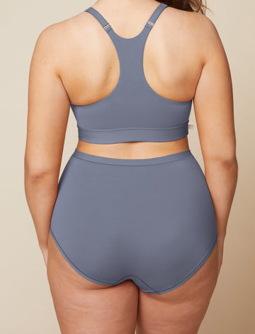 On a neutral beige backdrop, a back view of Summerlyn wearing the Bliss Boyshort in Steel highlights the full-coverage back and smooth, high-rise waistband.