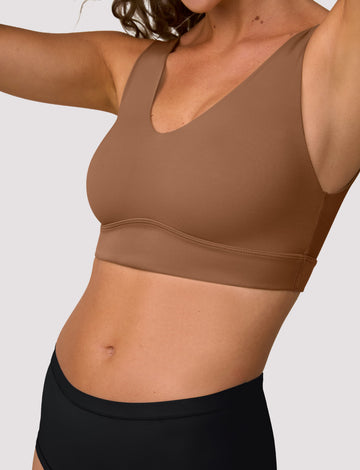 On a light studio backdrop, Freya wears the Bliss Bralette in Brown, shown in a close-up. The bralette features a scoop neckline, wide straps, and soft, lightweight fabric. sizing: Freya wears size Small