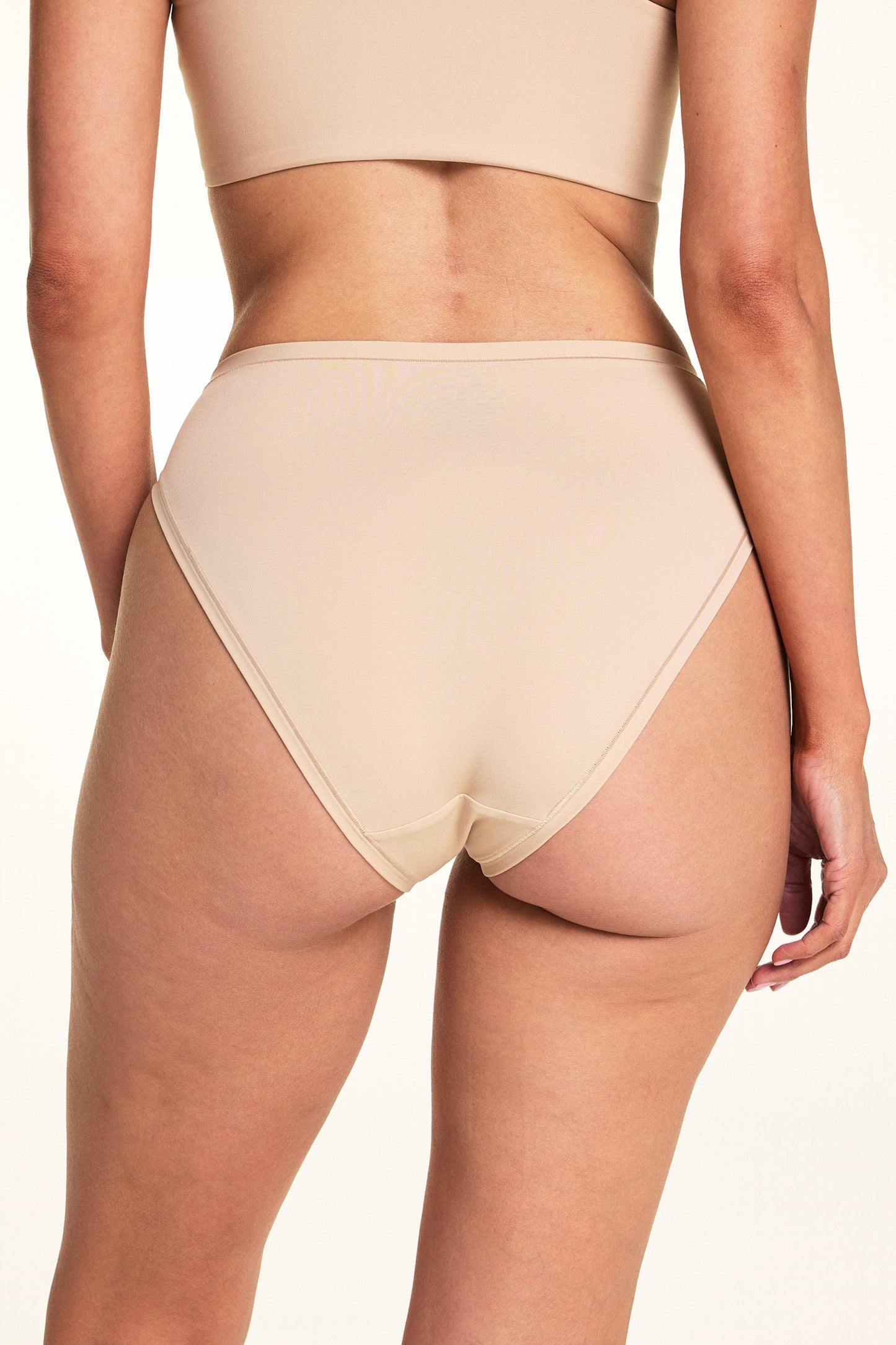 Against a white studio backdrop, Meagan wears the Bliss French Cut underwear in Beige, showing the back coverage and smooth waistband in a close-up back-facing pose.