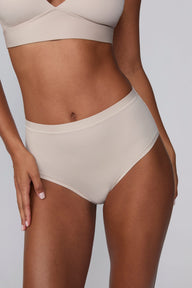 In a studio setting, Courtney wears the Bliss Highwaist Brief in Pebble. A close-up front view highlights the smooth fabric, high-rise waist, and clean finish.
