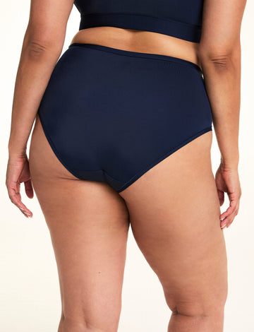 On a light studio backdrop, Jennifer is shown from the back wearing the Bliss Highwaist in Navy. The close-up highlights the full-coverage back, smooth fabric, and clean leg openings.