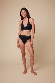 On a neutral beige backdrop, Anna wears the Bliss Lace Highwaist Thong in Black with the matching Bliss Lace Bralette, highlighting the high-waisted fit and lace-trim waistband in a full-body view.