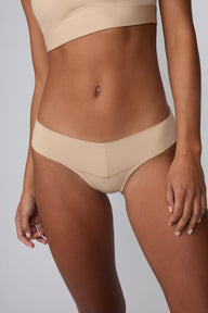 In a studio setting, Amber wears the Bliss Low Rise Bikini in Beige with the matching Bliss Bralette in Beige. A close-up front view highlights the low-rise waistband, smooth construction, and bikini coverage.