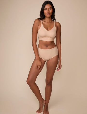 On a neutral studio backdrop, Victoria wears the Bliss Nursing Bralette in Beige with matching underwear. The full-body view showcases the bralette’s wireless construction, nursing clips, smooth silhouette, and wide comfort band.
