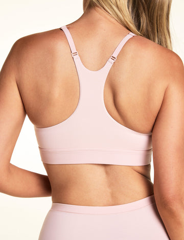 On a light studio backdrop, Meagan wears the Bliss Racerback Bralette in Ember Rose, shown from the back to highlight the racerback design, adjustable straps, and smooth back band.