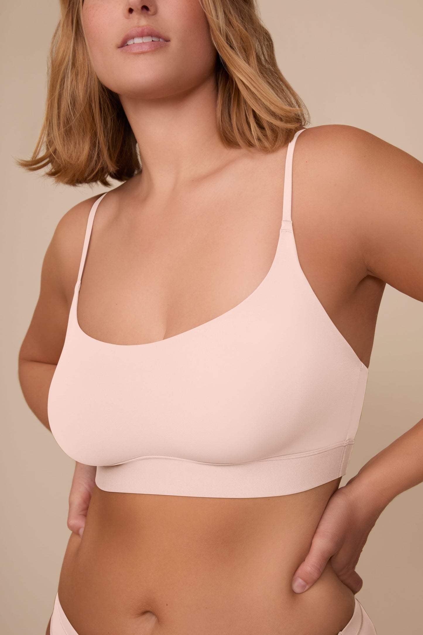 On a neutral beige backdrop, a close-up of Sonnie wearing the Bliss Scoop Adjustable Bralette in Rose highlights the scoop neckline, adjustable straps, and smooth, wireless design.