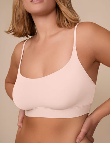On a neutral beige backdrop, a close-up of Sonnie wearing the Bliss Scoop Adjustable Bralette in Rose highlights the scoop neckline, adjustable straps, and smooth, wireless design.