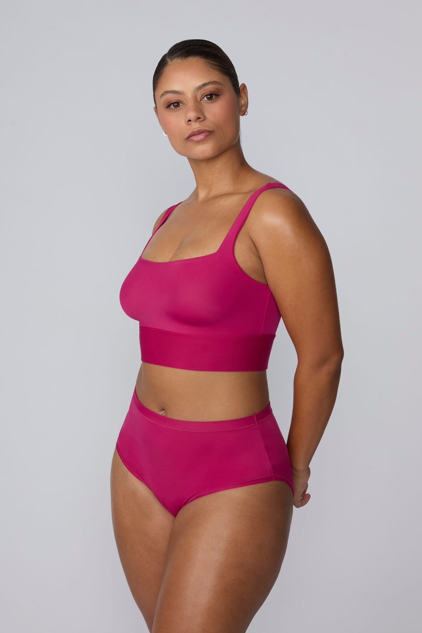 On a light gray studio backdrop, India wears the Bliss Square Neck Bralette in Winterberry with matching underwear. The angled full-body view highlights the square neckline, wide straps, and wide underband designed for comfortable support.