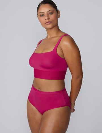 On a light gray studio backdrop, India wears the Bliss Square Neck Bralette in Winterberry with matching underwear. The angled full-body view highlights the square neckline, wide straps, and wide underband designed for comfortable support.
