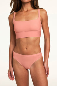 Against a neutral studio backdrop, Alana wears the Bliss Thong in Cabana with the matching Bliss bralette, featuring the low-rise silhouette, minimal coverage, and smooth finish.