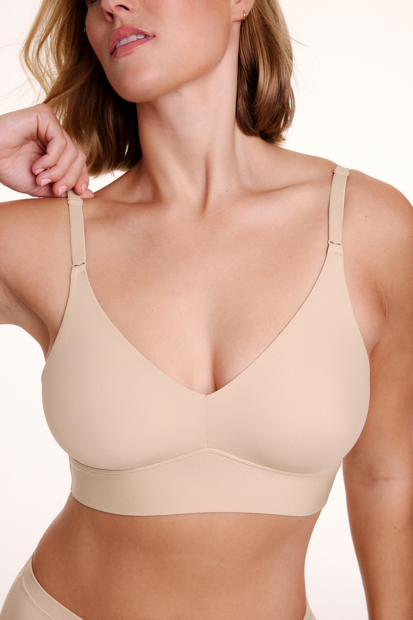 Close up view of Sonnie wearing the Bliss Triangle Bralette in Beige showing the deep V neckline, smooth microfiber fabric, and front adjusting straps. sizing: Sonnie wears size Large
