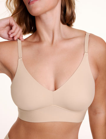 Close up view of Sonnie wearing the Bliss Triangle Bralette in Beige showing the deep V neckline, smooth microfiber fabric, and front adjusting straps. sizing: Sonnie wears size Large