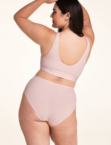 On a white studio backdrop, Alessandra wears the Bliss Bralette in Champagne Fizz from the back with arms raised, showing the scoop-back design and adjustable straps.
