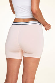 On a light studio backdrop, Meagan wears the Cloud Cotton Boxer Brief in Dogwood with a white tank top. The back view highlights the full-coverage boxer brief silhouette, smooth fabric, and striped elastic waistband.