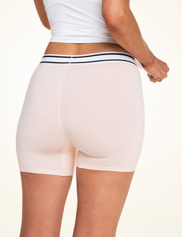 On a light studio backdrop, Meagan wears the Cloud Cotton Boxer Brief in Dogwood with a white tank top. The back view highlights the full-coverage boxer brief silhouette, smooth fabric, and striped elastic waistband.