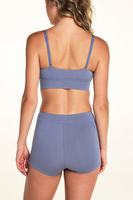 On a white studio backdrop, Alexis wears the Cloud Cotton Boyshort in Slate from the back, showing the full coverage seat and adjustable bralette straps above.