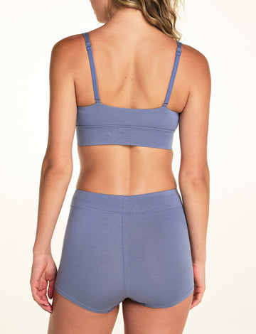 On a white studio backdrop, Alexis wears the Cloud Cotton Boyshort in Slate from the back, showing the full coverage seat and adjustable bralette straps above.