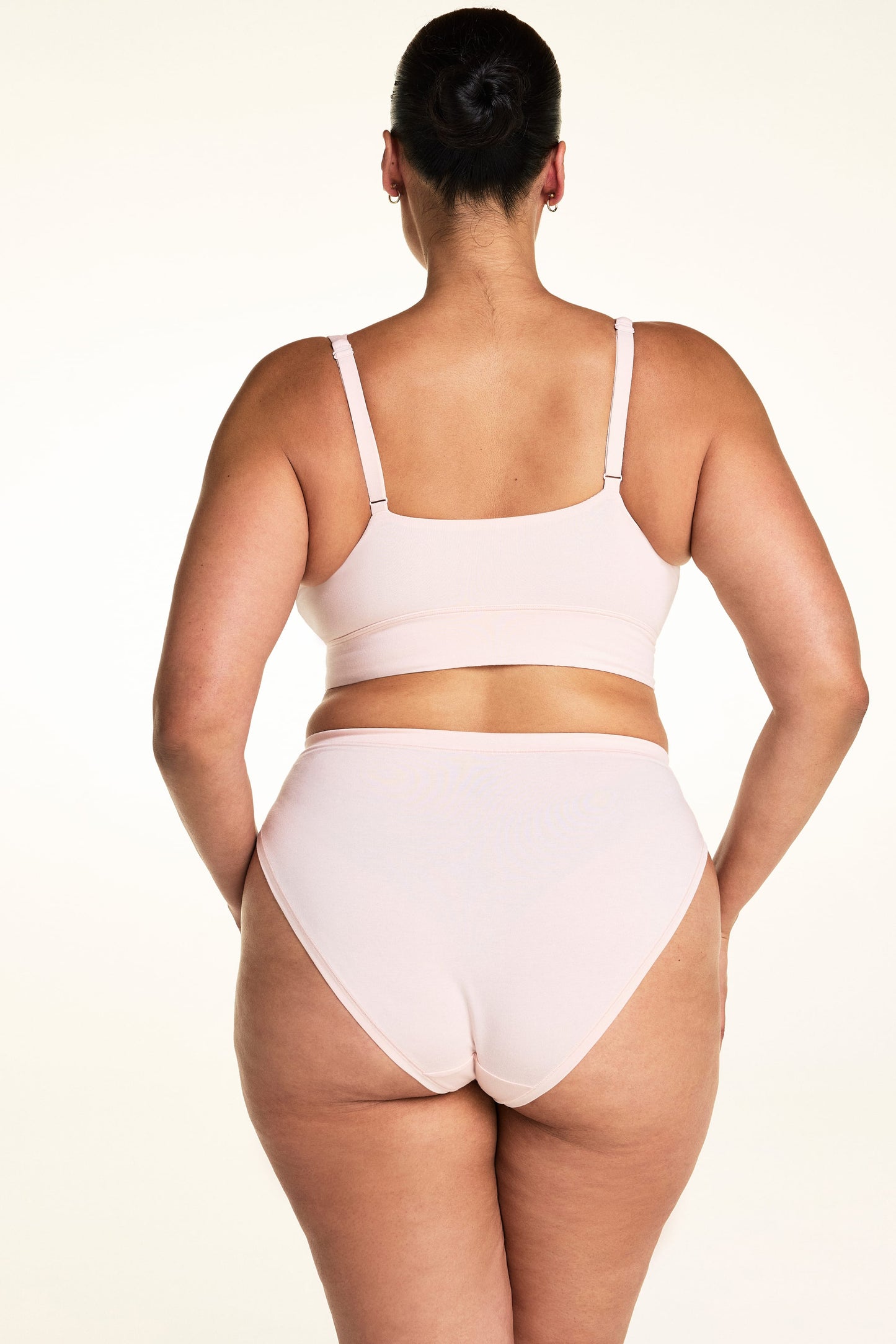 On a light studio backdrop, Jennifer wears the Cloud Cotton French Cut in Dogwood with the Bliss Triangle Bralette in Dogwood. The back view highlights the full back coverage, smooth waistband, and soft cotton fabric.