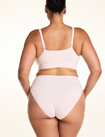On a light studio backdrop, Jennifer wears the Cloud Cotton French Cut in Dogwood with the Bliss Triangle Bralette in Dogwood. The back view highlights the full back coverage, smooth waistband, and soft cotton fabric.
