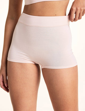 On a light studio backdrop, Laura wears the Cloud Cotton Highwaist Boyshort in Dogwood. The close-up highlights the high-rise waistband, smooth fabric, and full-coverage fit as she gently pulls the waistband outward.