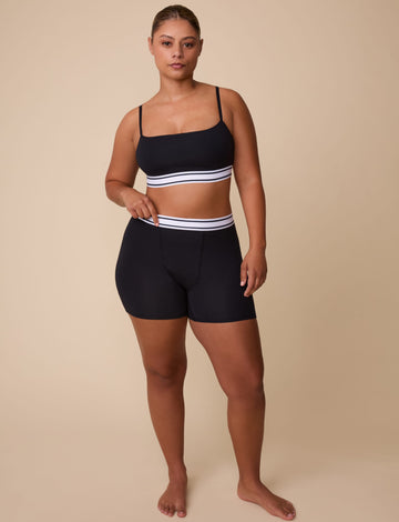 On a neutral studio backdrop, India wears the Cloud Cotton Retro Bandeau Bralette and Cloud Cotton Retro Boxer Brief in Black. She stands facing forward, showcasing the square neckline, thin adjustable straps, and coordinating retro logo waistbands. The boxer brief’s full-coverage silhouette and smooth cotton modal fabric are clearly visible.