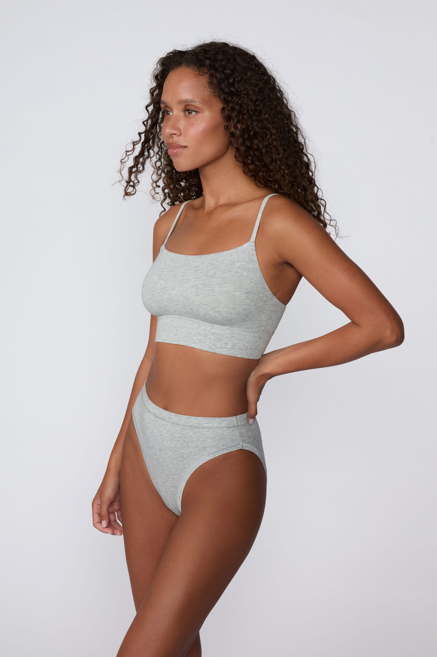 In a studio setting, Courtney wears the Cloud Cotton Thin Strap Bralette in Heather Grey with matching underwear. The side-angle view highlights the straight neckline, thin straps, and smooth cotton fabric.