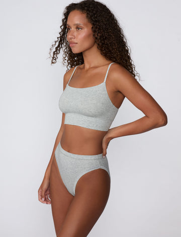 In a studio setting, Courtney wears the Cloud Cotton Thin Strap Bralette in Heather Grey with matching underwear. The side-angle view highlights the straight neckline, thin straps, and smooth cotton fabric.