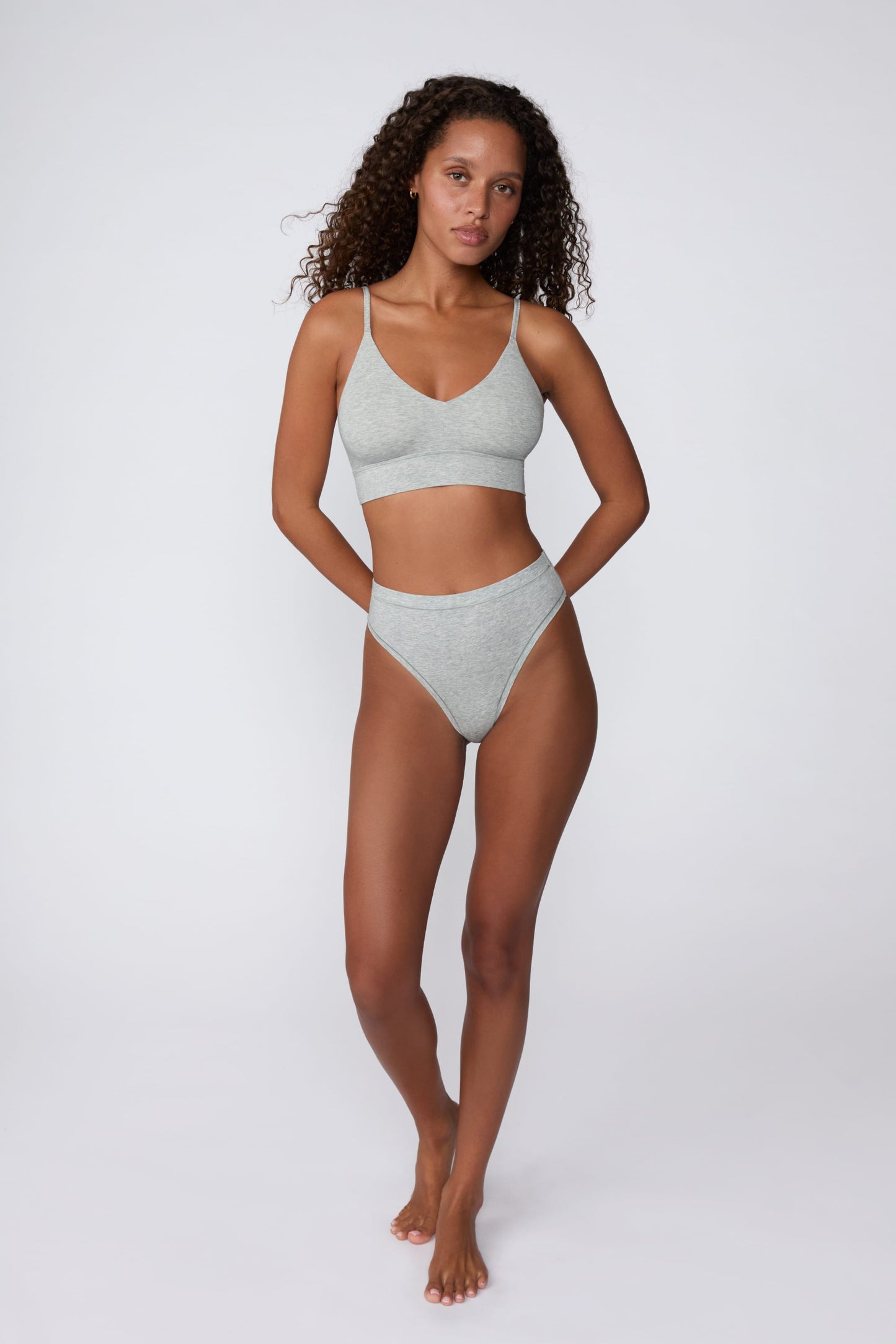In a studio setting, Courtney wears the Cloud Cotton Triangle Bralette in Heather Grey with matching underwear. The full-body view highlights the soft cotton fabric, deep V-neckline, and wide underband.
