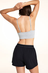 On a light studio backdrop, Laura wears the Cloud Cotton Plunge Bralette in Heather Grey with the Cloud Cotton Short in Black. The back view highlights the adjustable straps, soft heathered fabric, and wide comfort band.