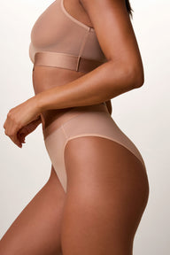 On a light studio backdrop, Ally wears the ComfortMesh™ Highwaist Brief in Taupe with the matching ComfortMesh™ Scoop Bralette. Shown from a side angle, the brief features sheer mesh fabric, a high-rise fit, and a smooth waistband.
