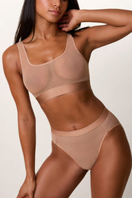 On a light studio backdrop, Ally wears the ComfortMesh™ Scoop Bralette in Taupe with the matching brief. The sheer mesh fabric, scoop neckline, and wide comfort band are shown in a full-body angled view.
