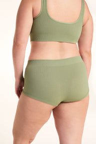On a white studio backdrop, Alessandra models the back of the Lounge Rib Sleepshort in Dill with the matching Lounge Rib bralette, showing the ribbed fabric, seamless construction, and full back view.