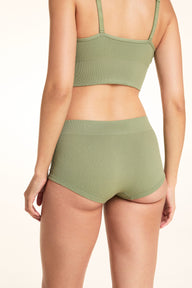 On a white studio backdrop, Laura models the back of the Lounge Rib Sleepshort in Dill, showing the ribbed fabric, seamless construction, and full back view.