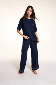 Against a neutral studio backdrop, Meagan wears the Perfect Pima Pant Set in Navy, featuring a relaxed short-sleeve sleep tee with a chest pocket and matching wide-leg lounge pants with contrast piping at the hem. sizing: Laura wears size Small