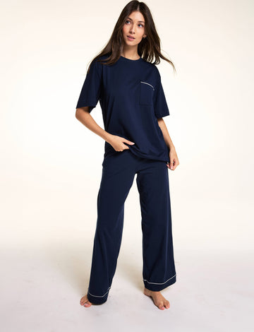 Against a neutral studio backdrop, Meagan wears the Perfect Pima Pant Set in Navy, featuring a relaxed short-sleeve sleep tee with a chest pocket and matching wide-leg lounge pants with contrast piping at the hem. sizing: Laura wears size Small