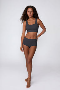 On a light gray studio backdrop, Courtney wears the Ribbed Seamless Boyshort in Charcoal with a matching ribbed bralette. A full-body view highlights the high-rise waistband, boyshort silhouette, and ribbed texture.