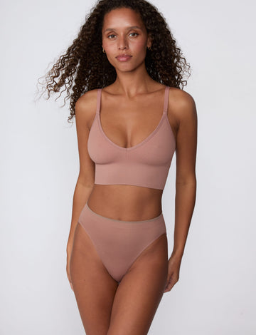 In a studio setting, Courtney wears the Smooth Seamless Brief in Plum with the matching Seamless Scoop Bralette in Plum. The front view highlights the high-leg cut, smooth finish, and comfortable coverage.