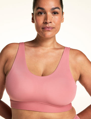 On a light neutral backdrop, Jennifer wears the Bliss Scoop Adjustable Bralette in Cinnamon. The close-up highlights the scoop neckline, wide adjustable straps, and smooth microfiber fabric with wireless support.