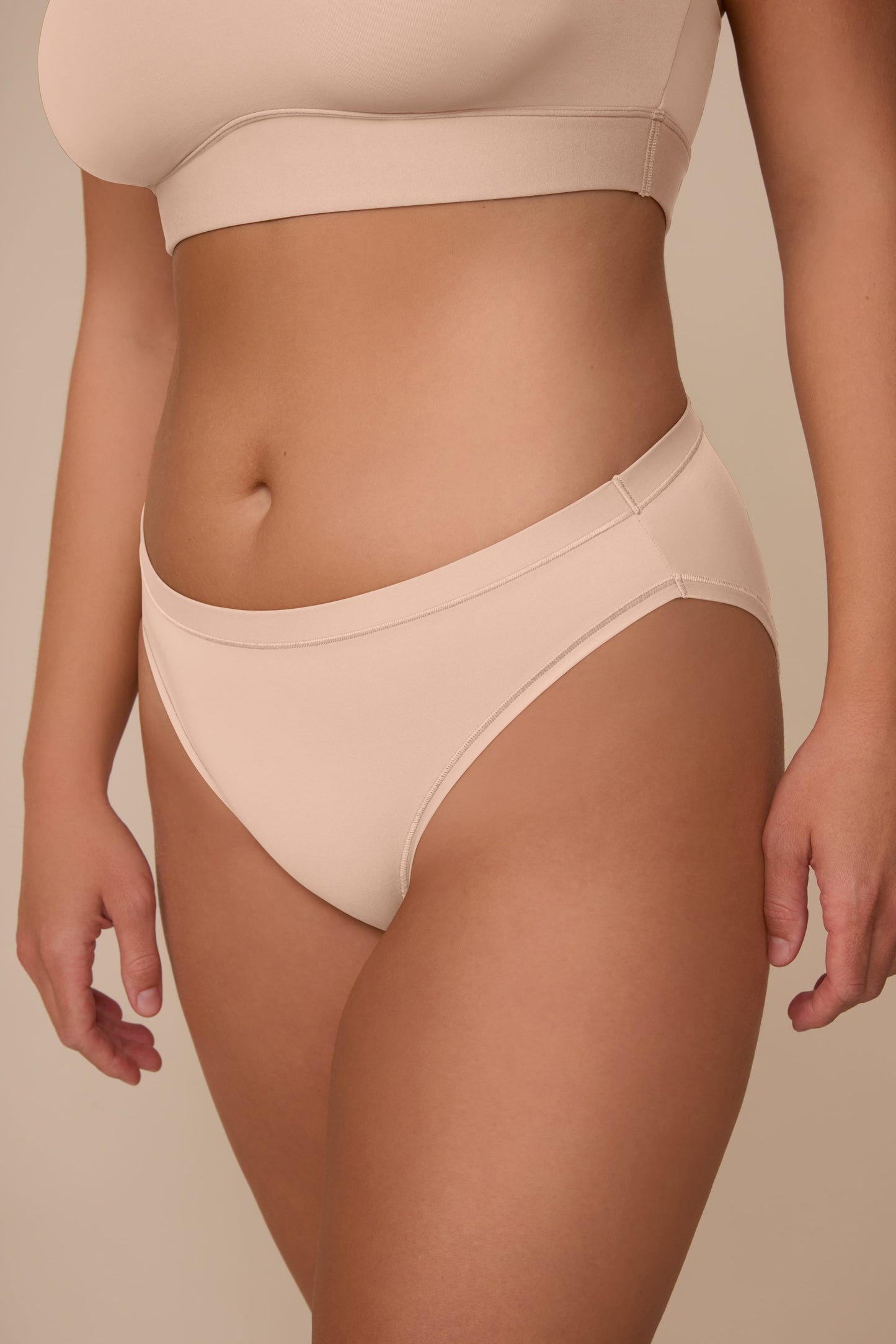 On a neutral beige backdrop, a close-up of the Bliss Bikini in Beige highlights the low-rise fit, smooth waistband, and soft fabric.